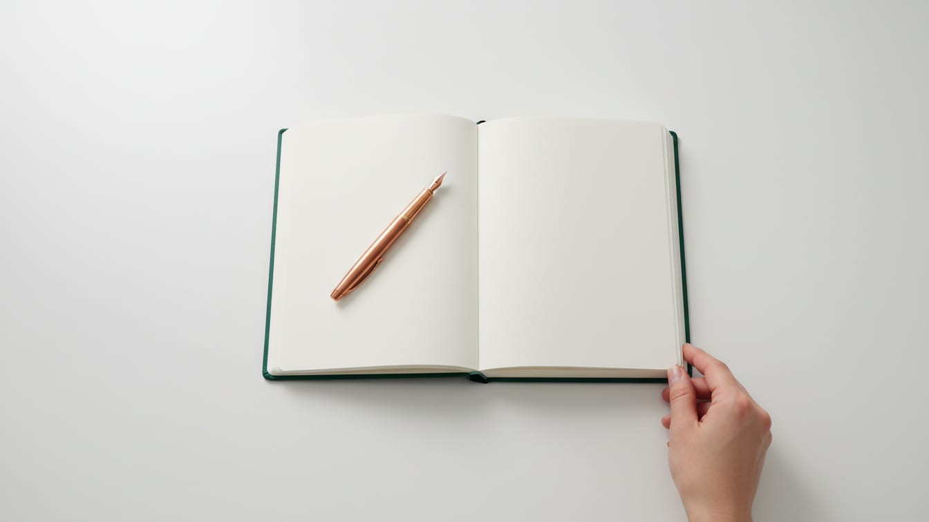 Illustration: An open notebook with a deep green cover and a copper fountain pen on a white desk.