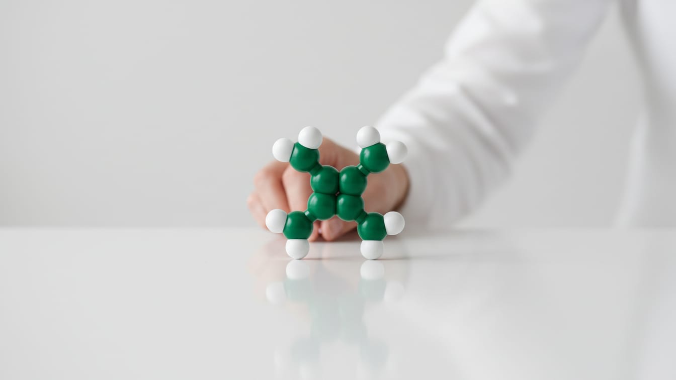 Illustration: An abstract ring-shaped peptide model in white and deep green on a white surface with copper reflections.