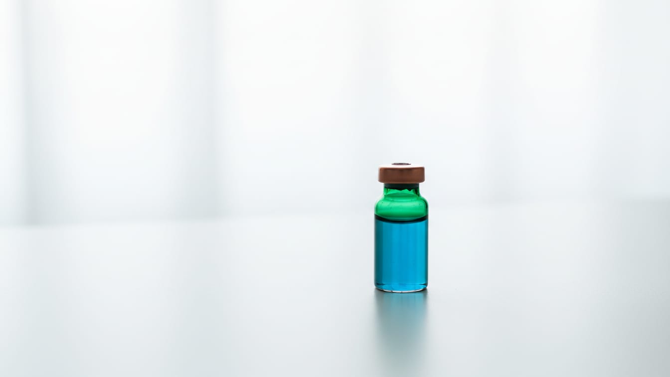 Illustration: A deep green glass vial with a blue liquid and a copper cap on a white desk.