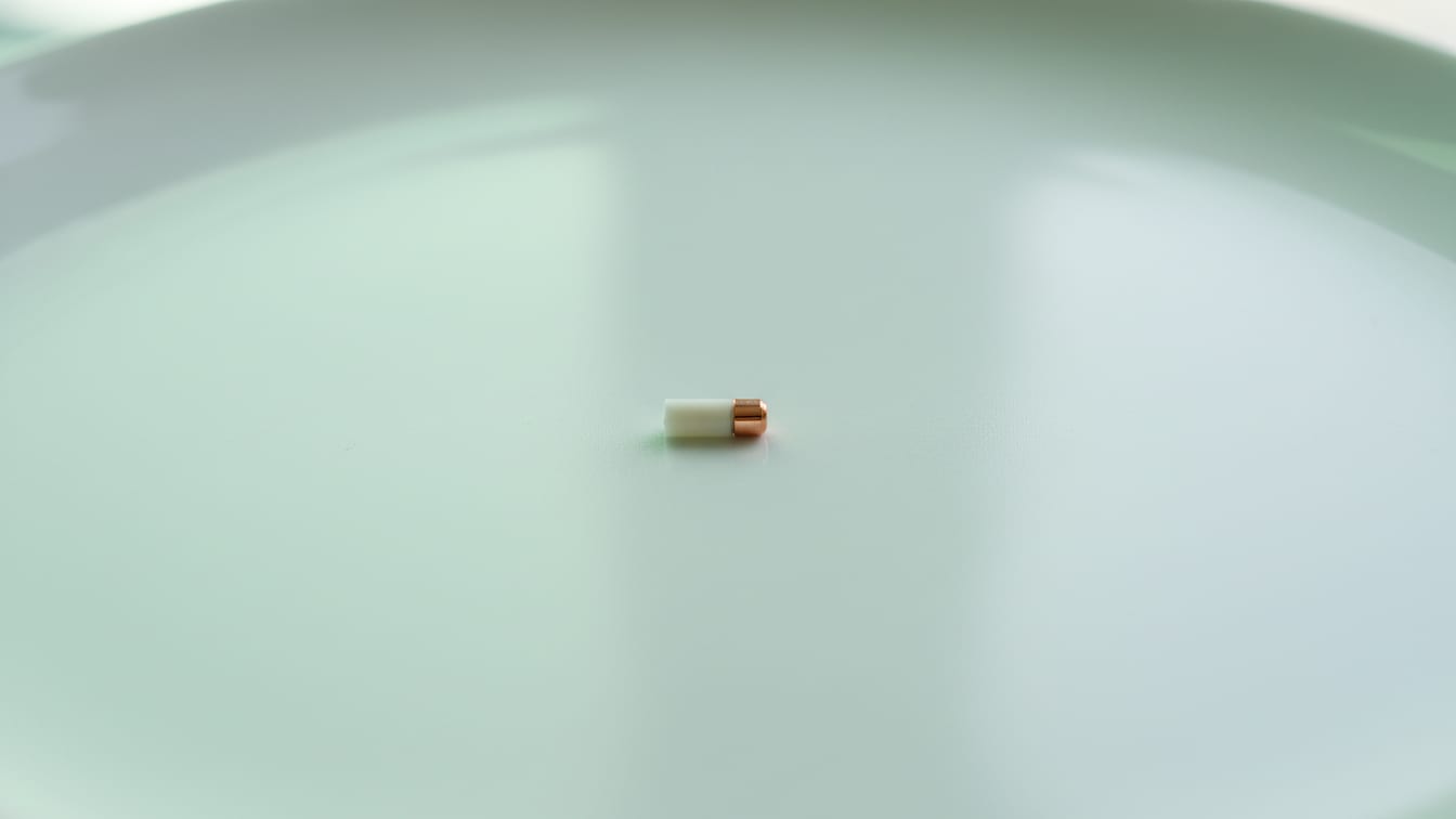 Illustration: A small, off-white cylindrical implant on a white surface with green and copper reflections.